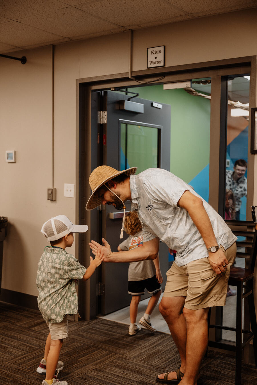 A leader greeting a small child at the door.