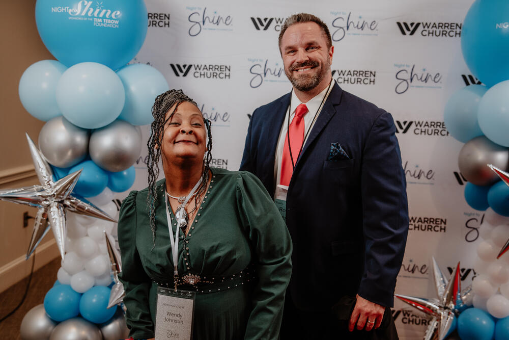 A guest and a volunteer at the backdrop.
