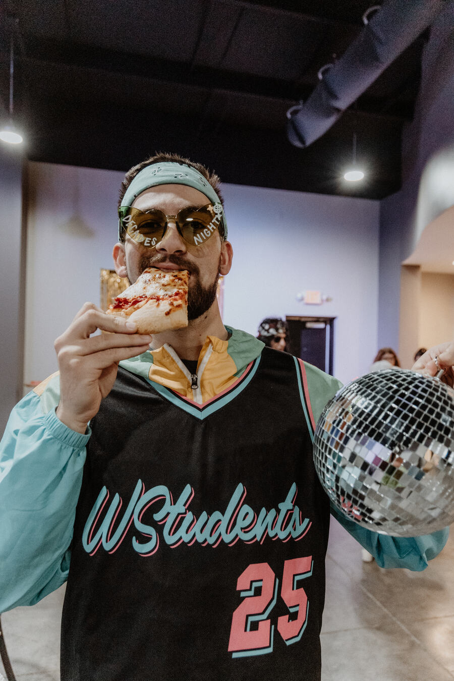 A student in a WStudents jersey with a slice of pizza.