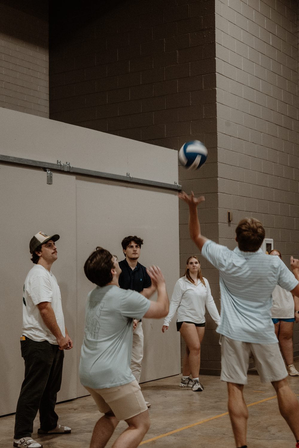 A volleyball rally in the gym, a player reaching for the ball.