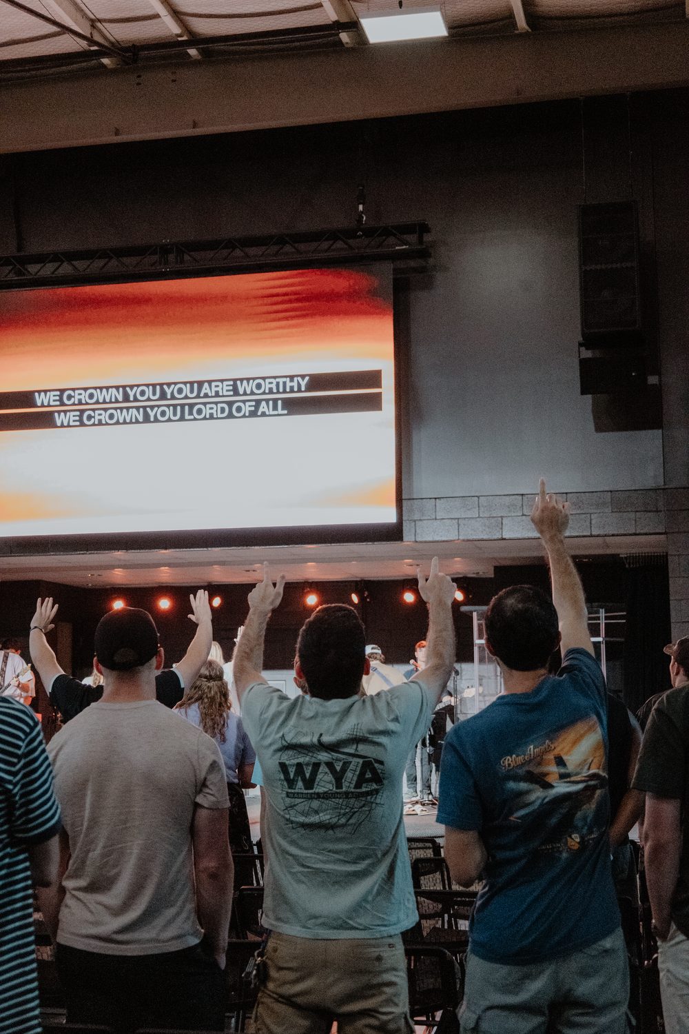 People standing with their hands raised, song words on the screen behind them.